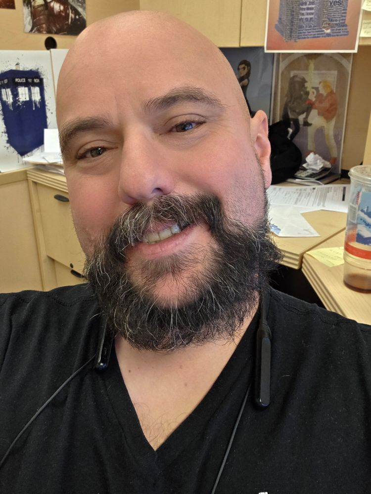 Nick smiles at camera in a black tank shirt. His beard is showing some salt and pepper.