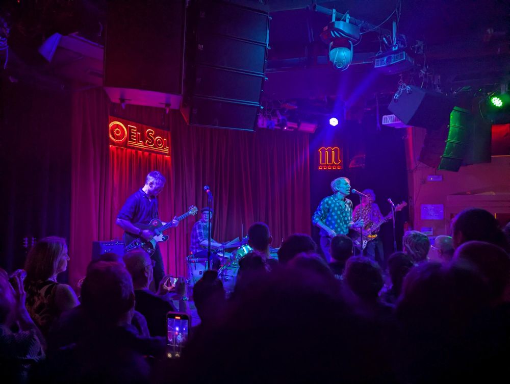 bamd playing at a stage with purple and blueish light tones.