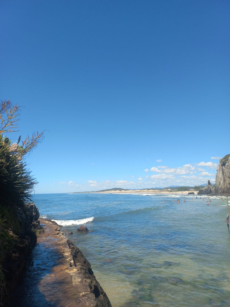 Foto do mar azul, sem ondas. Ao fundo a praia. 