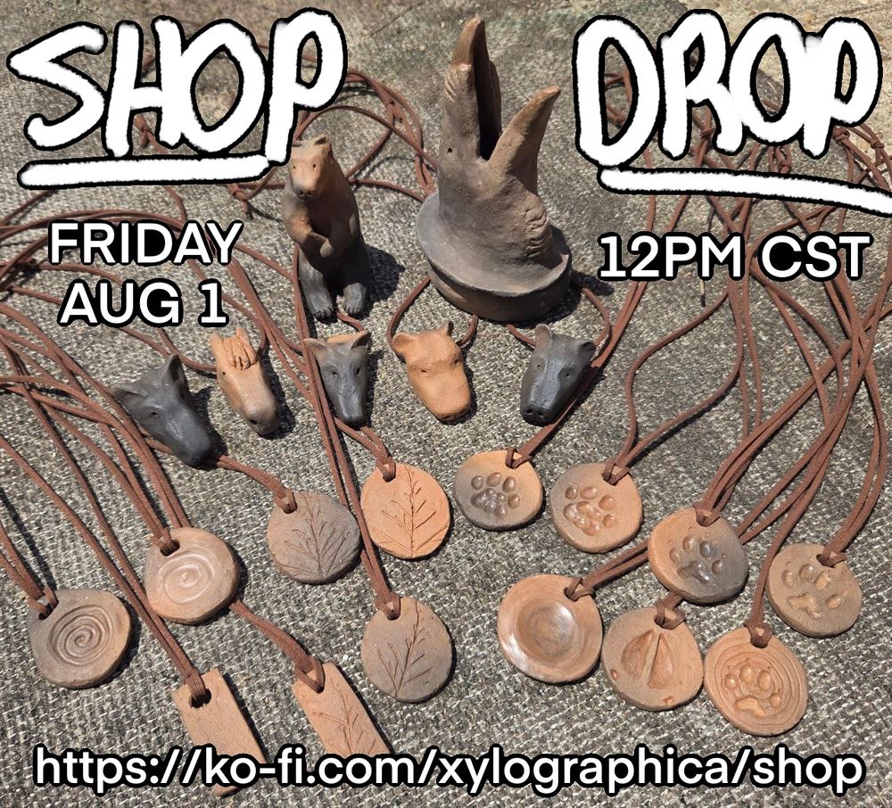 A photo of a variety of clay pendants and sculpture on a grey woven background. The clay is all mottled in shades of reddish brown, grey, and black. In the back is a sitting bear sculpture and a croaking raven incense burner. In front of them are five animal head pendants of various species. Around them are around a dozen flat clay pendants with designs including paw prints, spirals, and plant impressions. The pendants are all strung on brown leather cord