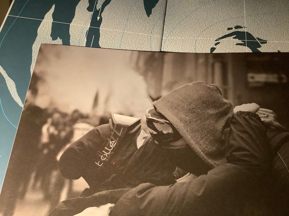 Deux personnes du bloc, en pleine manif, s’enlacent et s’embrassent sur les lèvres (à travers les écharpes, etc) - et dégagent beaucoup d’amour et de gaieté. Le grain de la photo est noir et blanc, avec une nuance jaune-cendre :))

La photo est posée sur une carte météorologique de cyclone, extraite de l’Atlas des nuages de Julie Guilhem.