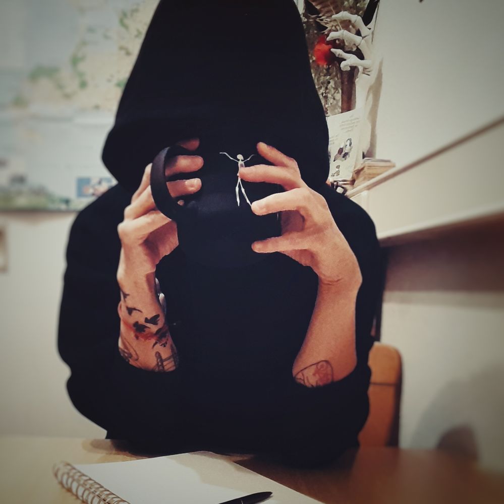 Userin, man sieht das Gesicht wegen der Kapuze und Kaffeetasse nicht. Vor ihr liegt ein Block mit Stift 