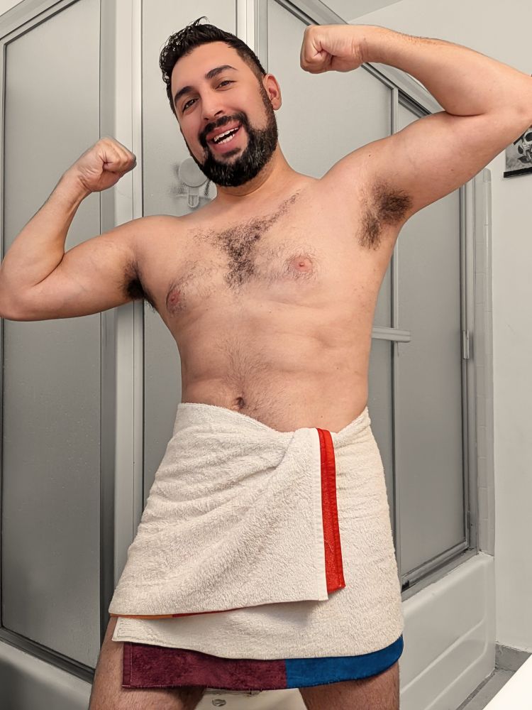 I'm flexing for the camera with a big smile on my face. I'm wearing only a small towel.