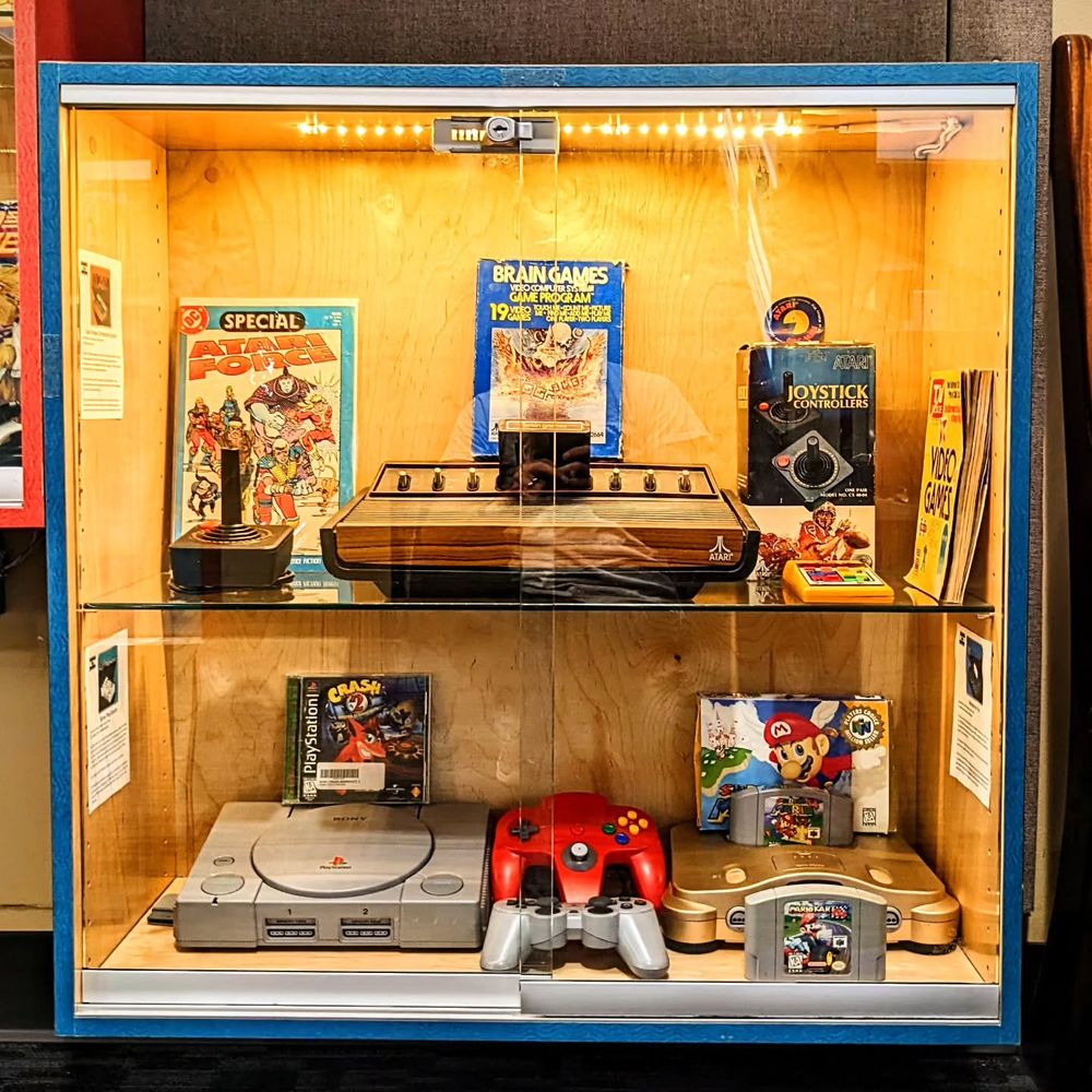 The last case has an Atari 2600 "heavy sixer" console, a PlayStation console, and a gold Nintendo 64 console. There are controllers and games for each of the systems.
