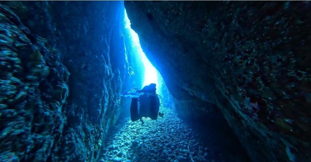 Un plongeur sort d'une grotte. Il est comme en suspension au dessus du fond