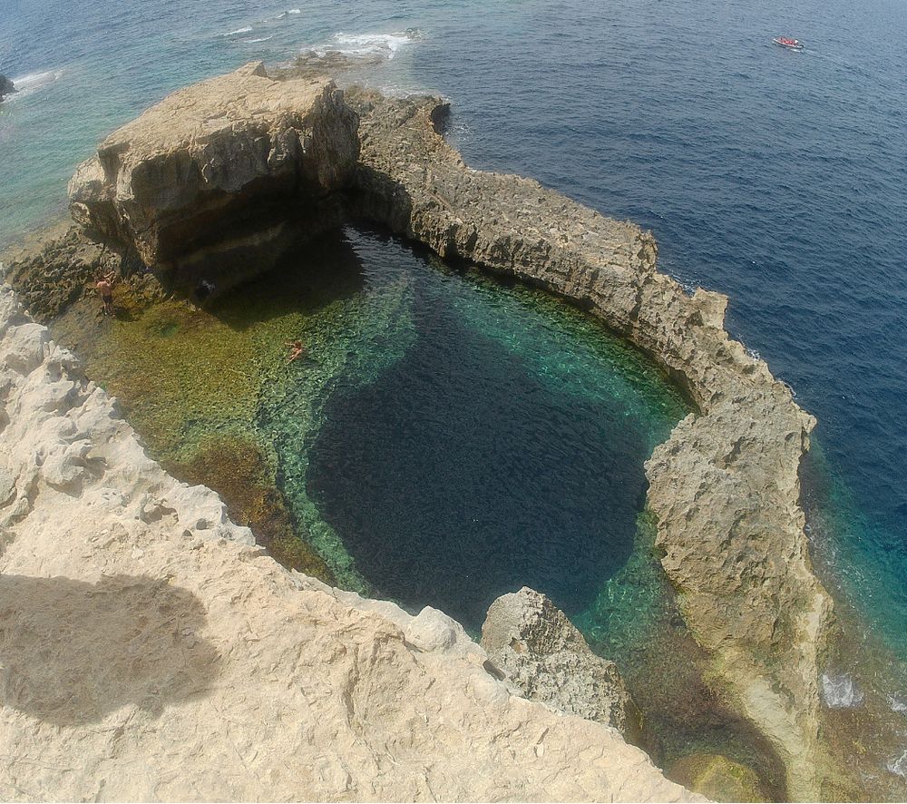 Depuis une falaise, en contre bas un trou bleu dans la mer entouré par une bande  rocheuse et l la côte