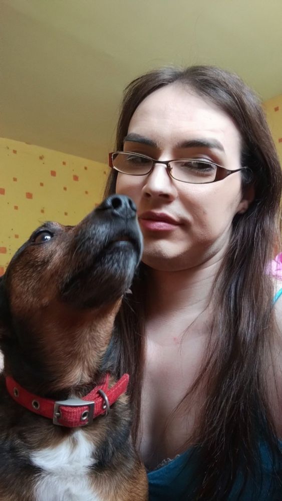 Selfie of the poster with glasses and long brown hair, with their little brown dog getting In the shot.