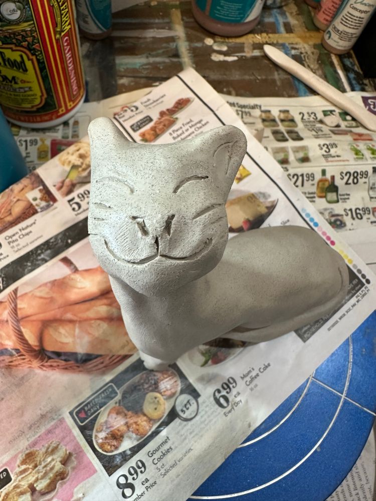 A cat in wet clay. The cat looks like it’s smiling. 