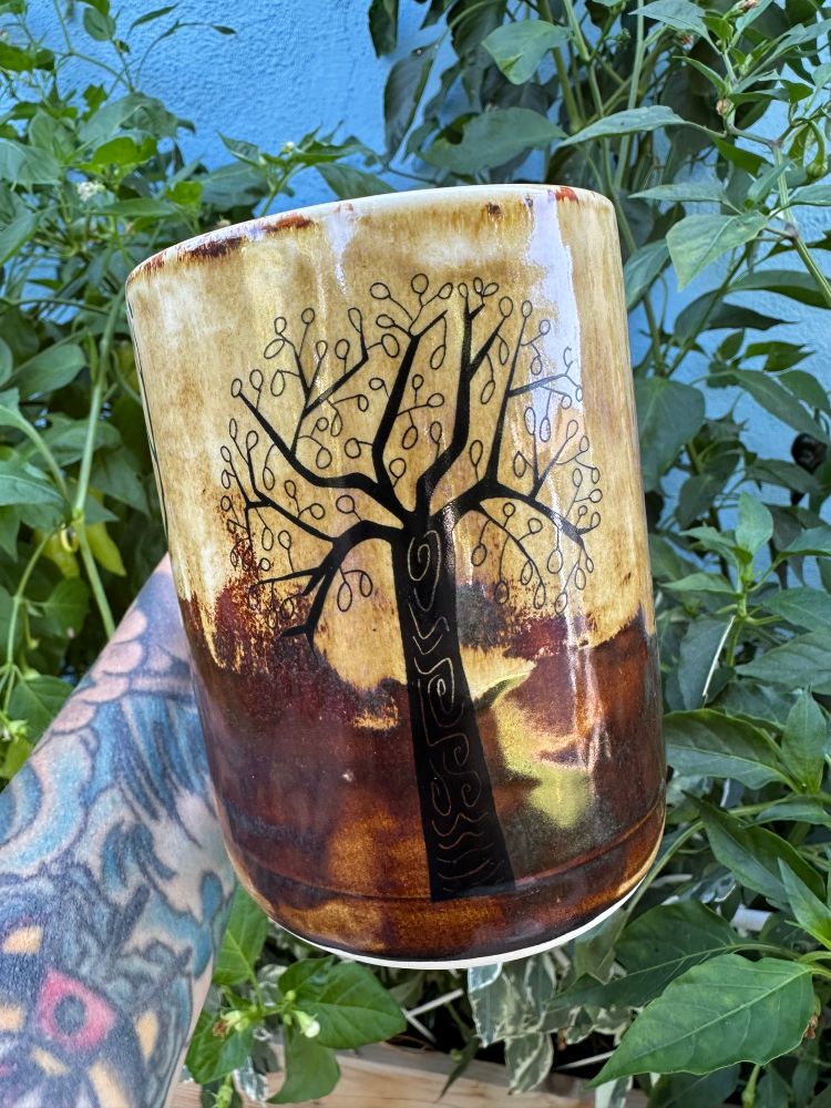 A multi shade of brown glazed mug with three different tree illustrations on it. This is like a fruit type tree. 