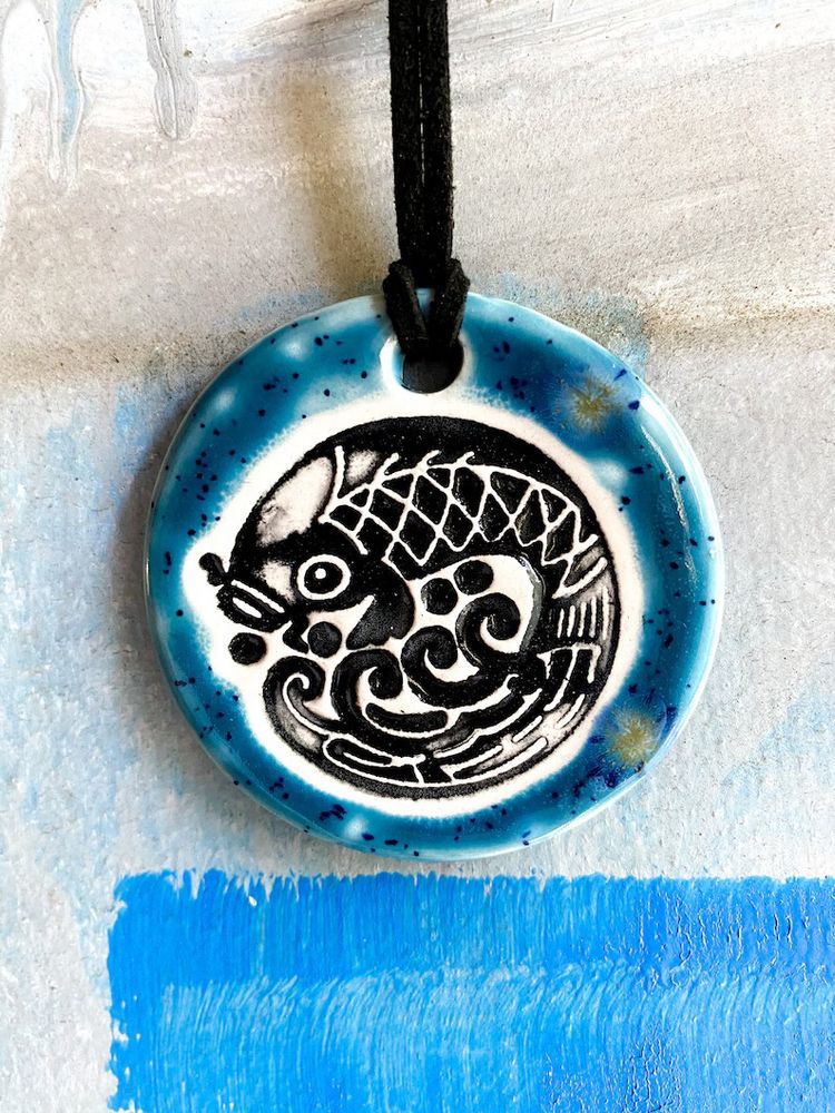 A round handmade ceramic pendant with a koi fish design. 