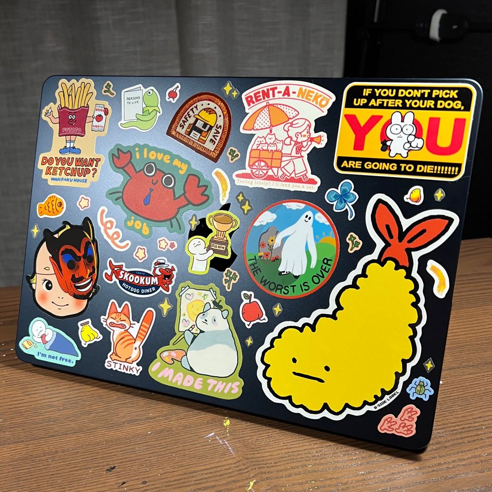A laptop, covered in cute stickers - a predominantly red/yellow/teal palette, that have funny slogans and silly characters.