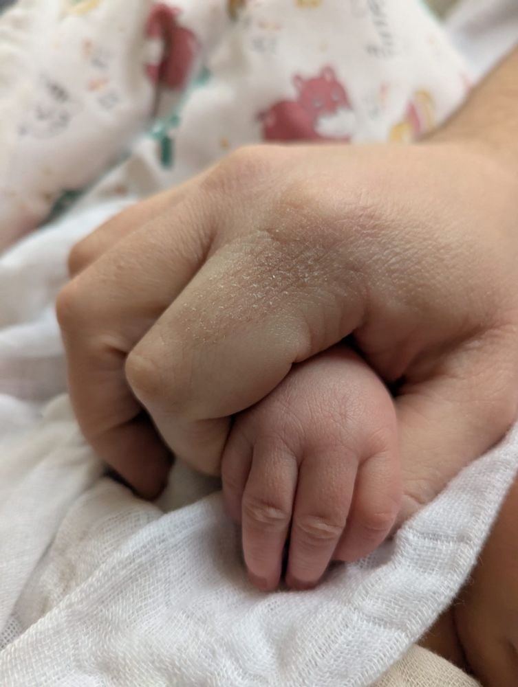 An adult hand (this user) holding the hand of a newborn (Samuel)