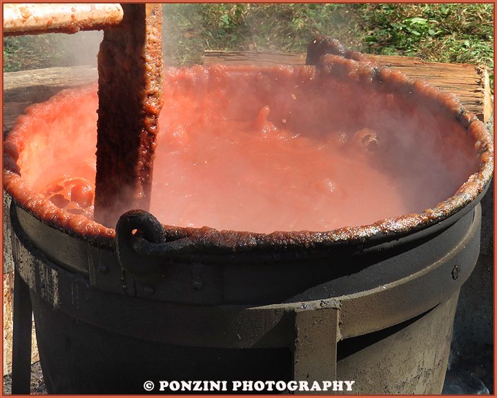 A large cauldron filled with the ingredients to make apple butter being stirred during the process.