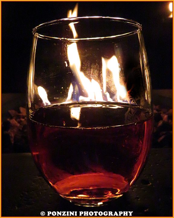 A glass of sangria sits in front of a cozy fire.