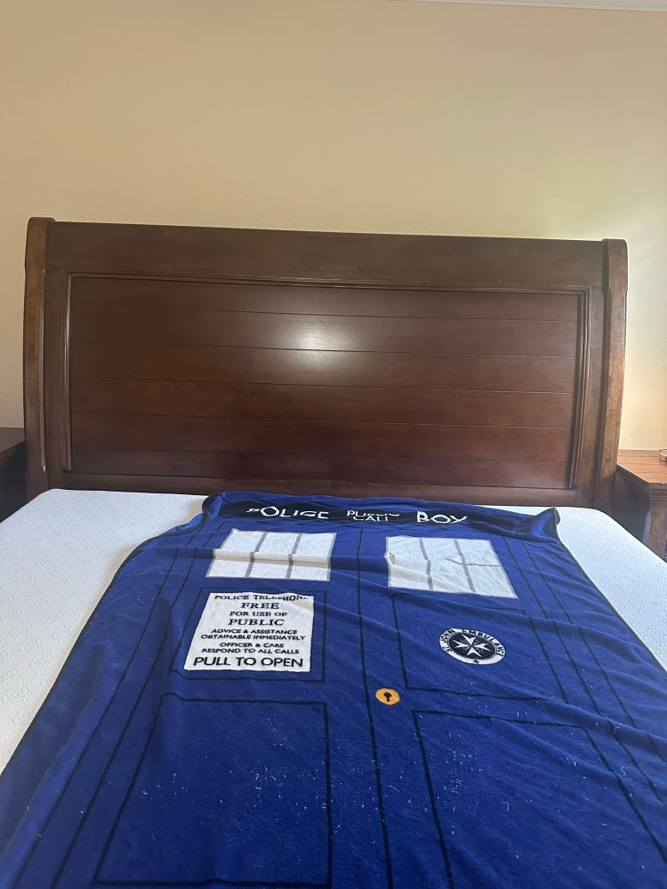 Large heavy wooden headboard with a TARDIS blanket on a mattress.