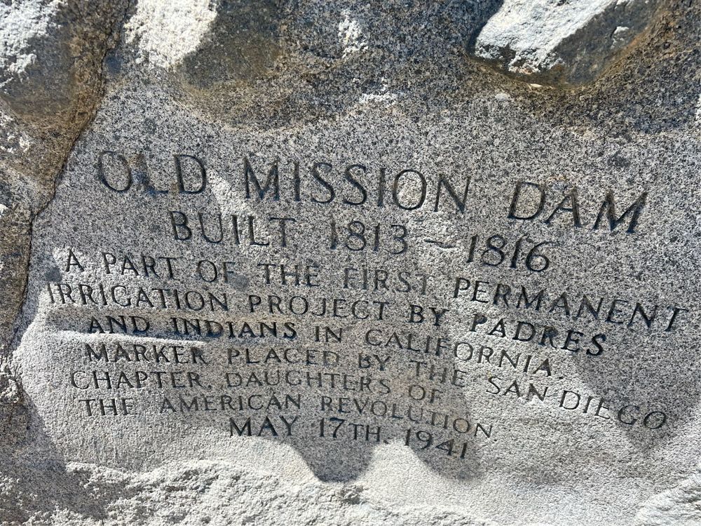 A rock inscribed with:

OLD MISSION DAM
BUILT 1813 - 1816
A PART OF THE FIRST PERMANENT IRRIGATION PROJECT BY PADRES AND INDIANS IN CALIFORNIA
MARKER PLACED BY THE SAN DIEGO
CHAPTER DAUGHTERS OF
THE
AMERICAN
REVOLUTION
MAY 17TH. 1941