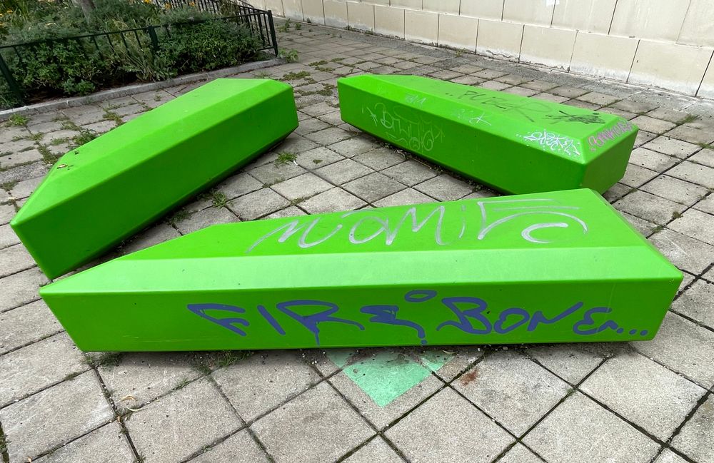 Purple spraypaint graffiti on green concrete benches reading “FIREBONEr”.