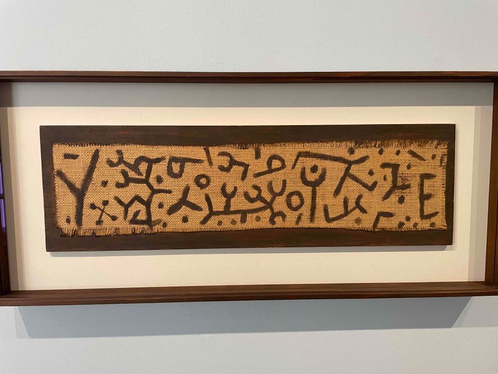 Some asemic script in black paint on a strip of burlap.