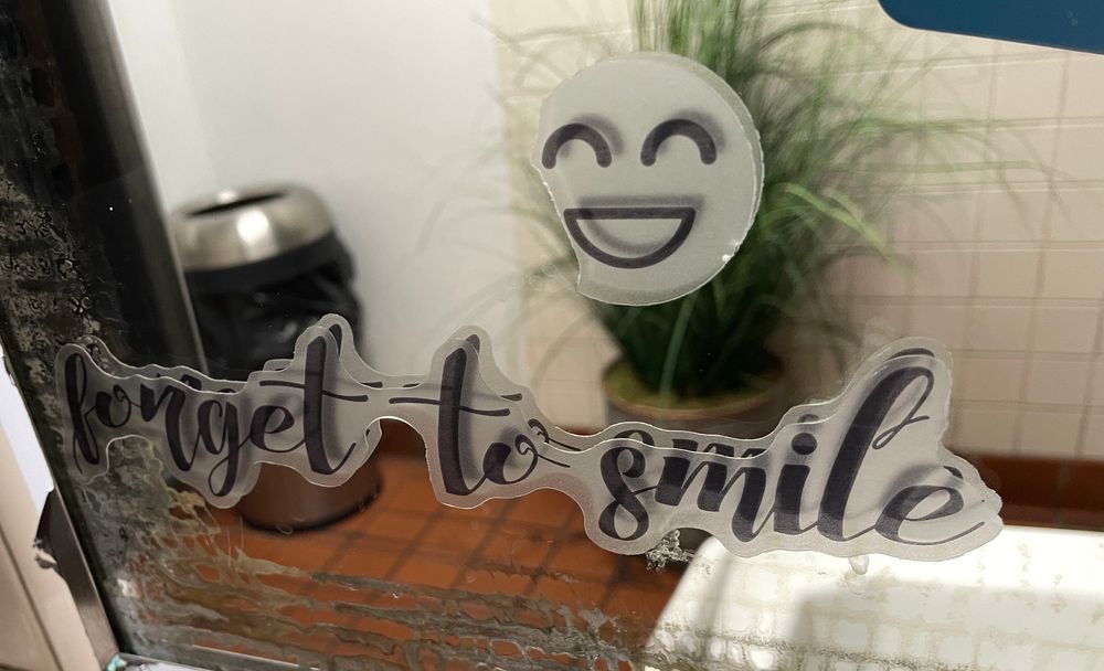 A mirror with a partial sticker saying “😄 forget to smile”.