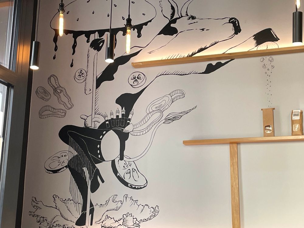 A black-and-white wall mural of a cow stripteasing between two hamburger buns 