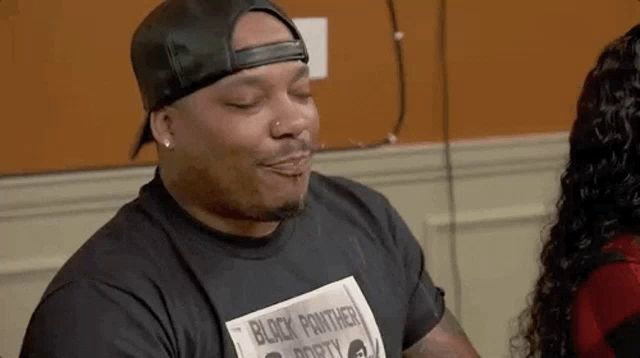 a man wearing a hat and a black panther t-shirt is sitting in front of a woman .