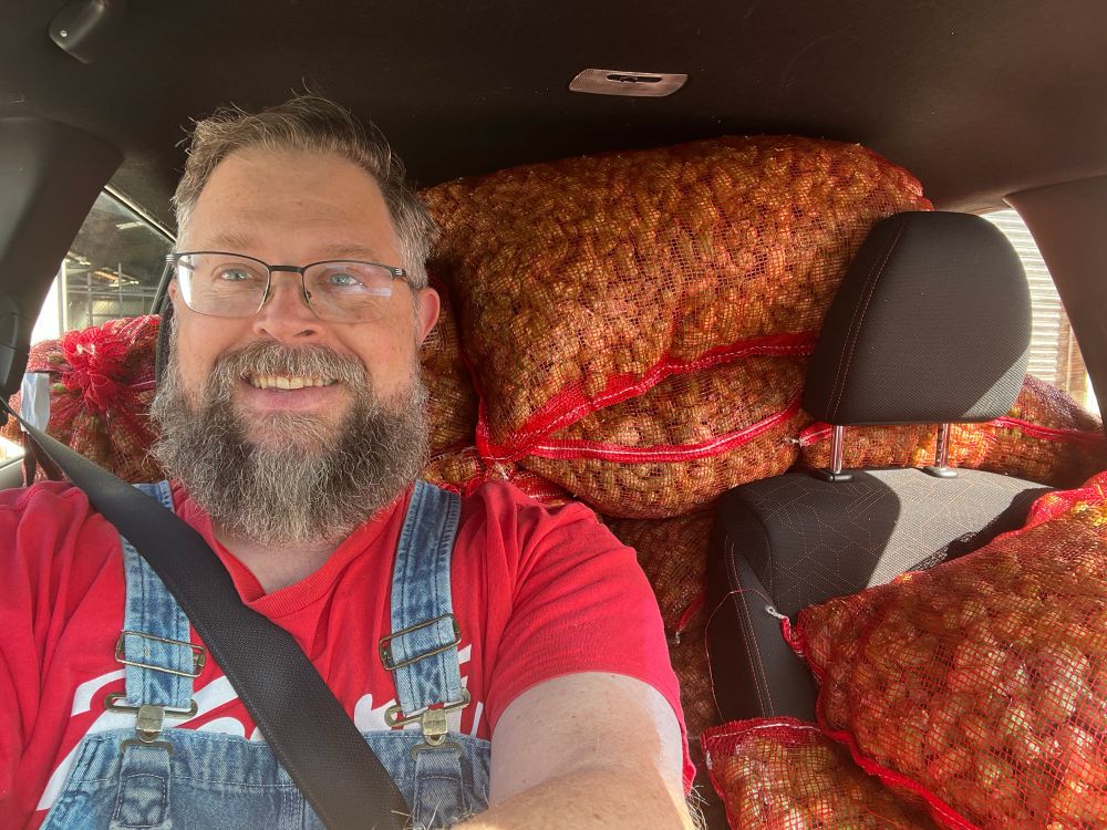 Brewer in a red t-shirt seated in a Honda Jazz and completely surrounded by bags of fresh hop cones.
