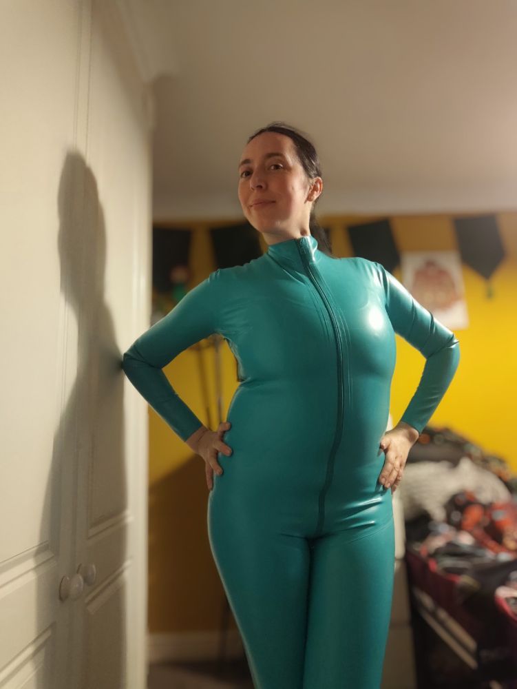 Lass in a turquoise latex catsuit with a yellow background