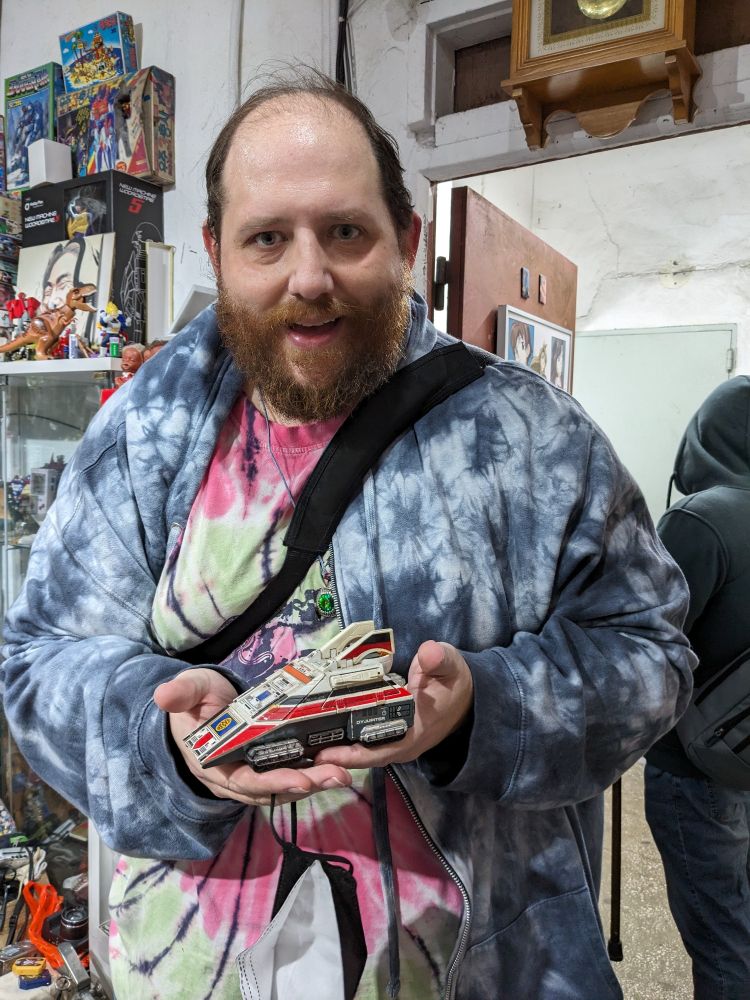 An awed and enthusiastic bearded person in a brightly colored tie-dyed t-shirt, holding up an original Dynajet from Dynaman in both hands.
