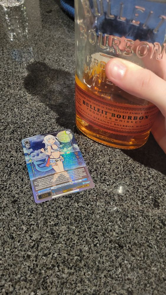Gawr Gura trading card next to a bottle of whiskey I'm holding