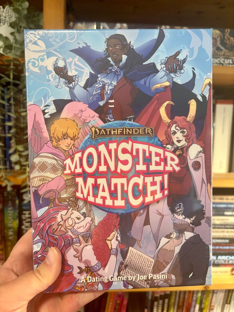 Pathfinder Monster Match by Joe Pasini, held up in front of a bookcase. The box features art of various hot monster people.