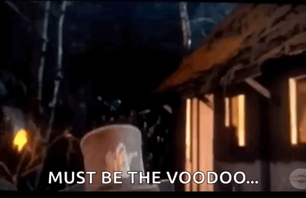 a man in a top hat is standing in front of a building with the words `` must be the voodoo '' written on it .