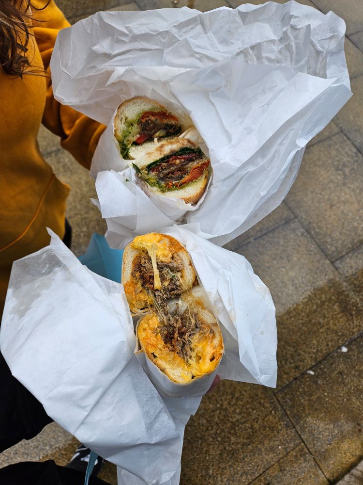 Two sandwiches wrapped up in paper held by two people