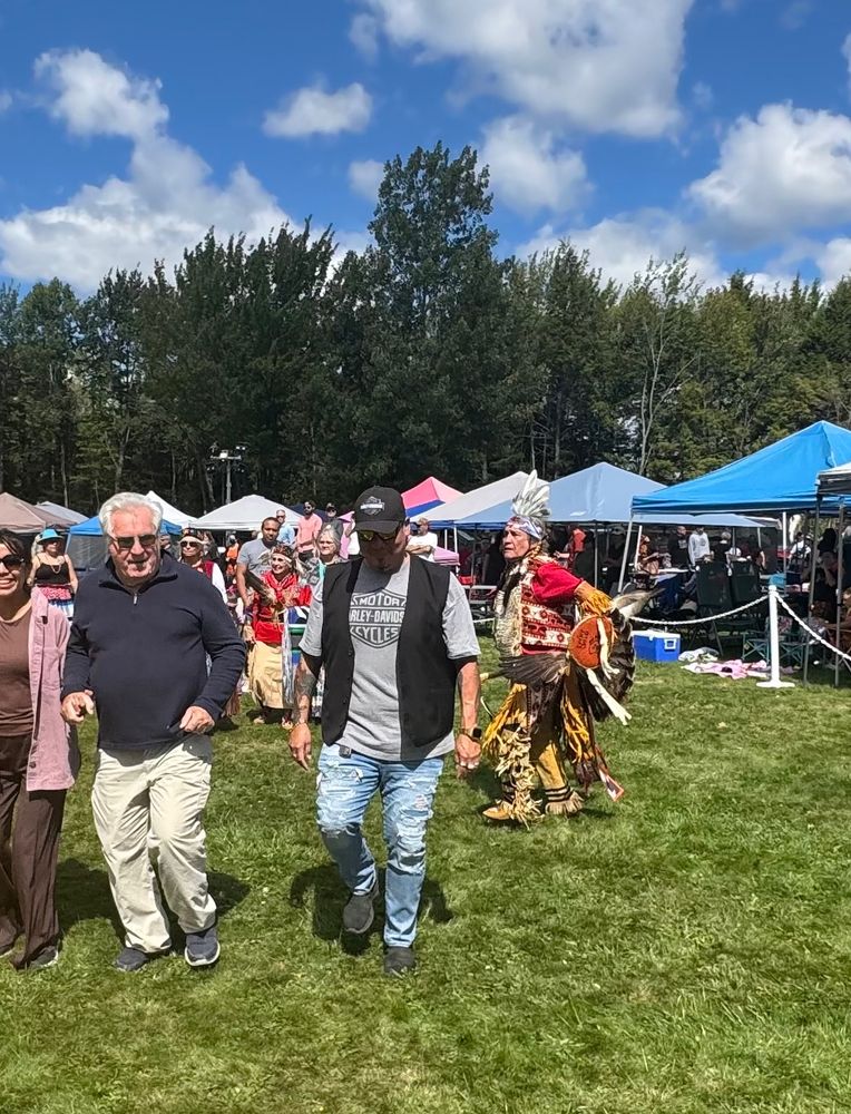 A ground of people dancing, with one man in traditional anishinaabe dance regalia 