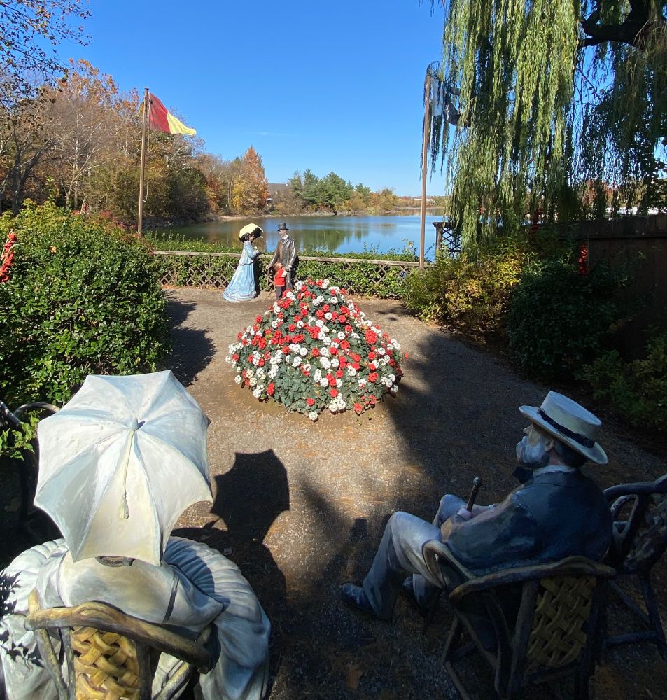 Lifelike statues of people in 19th century dress facing water