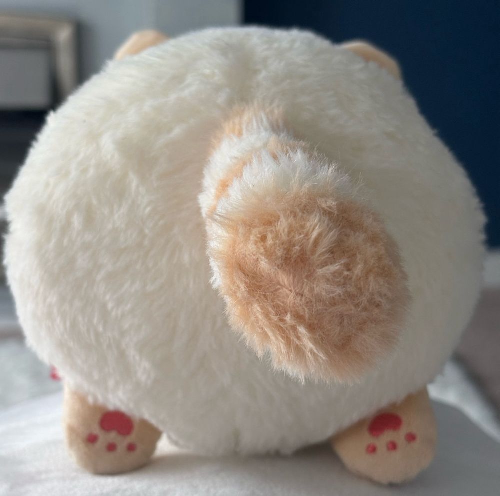 a picture of plush racoonlian from the back. his tail is striped white and light brown. his paws have three pink dots and a larger bean shape above them.