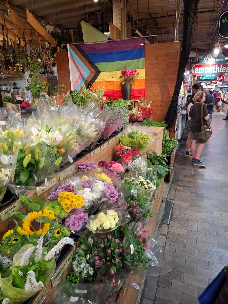 Picture taken at Philadelphia Reading Terminal Market showing a flower selling booth with a LGBTQ flag in the background. 