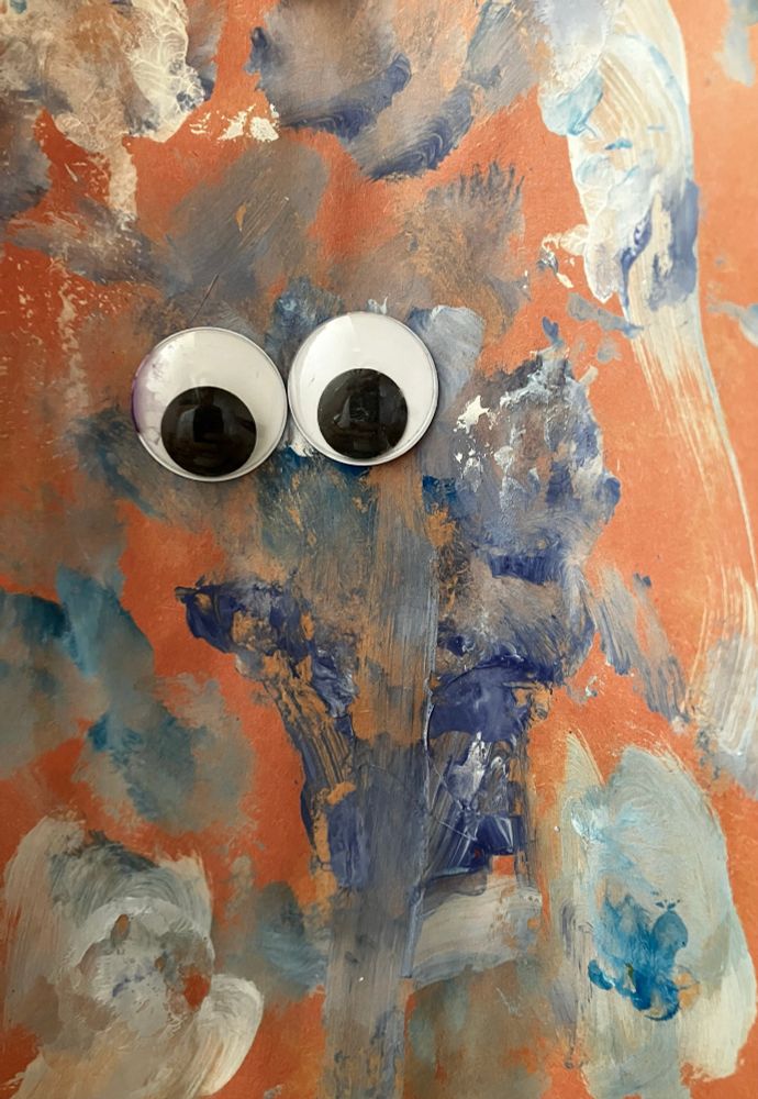 A painting by a then 3 year old that looks abstractly like Cookie Monster. It has blue and white paints done with (I think) fingers and sponges on a reddish-brown construction-paper canvas. There are two large googly eyes roughly where Cookie Monster’s eyes would go if this were actually meant to be Cookie Monster, which, c’mon, it definitely is. 