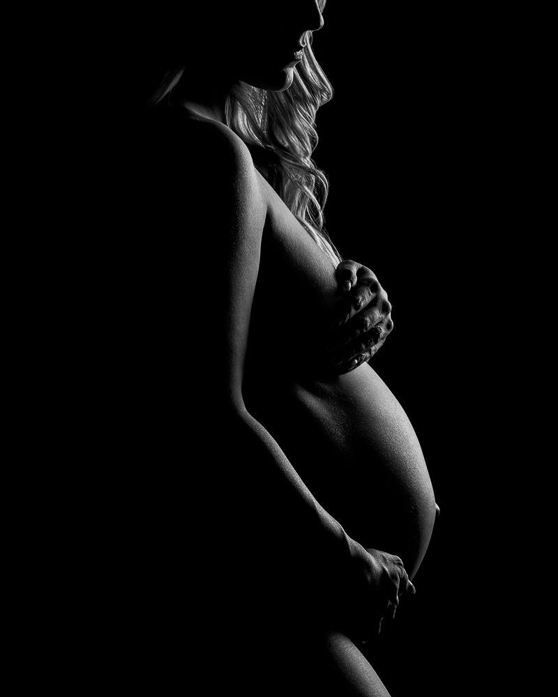 Dramatic silhouette of a pregnant woman holding her belly in profile during a maternity shoot