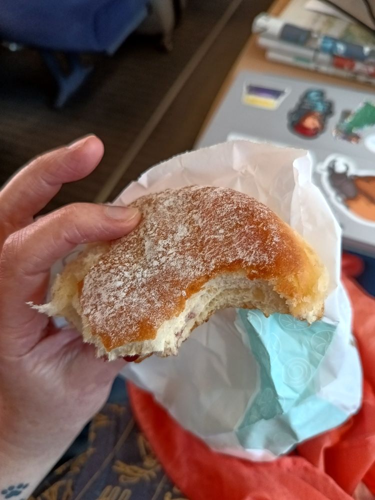 Roxane hält einen angebissenen Puderkrapfen in der Hand.