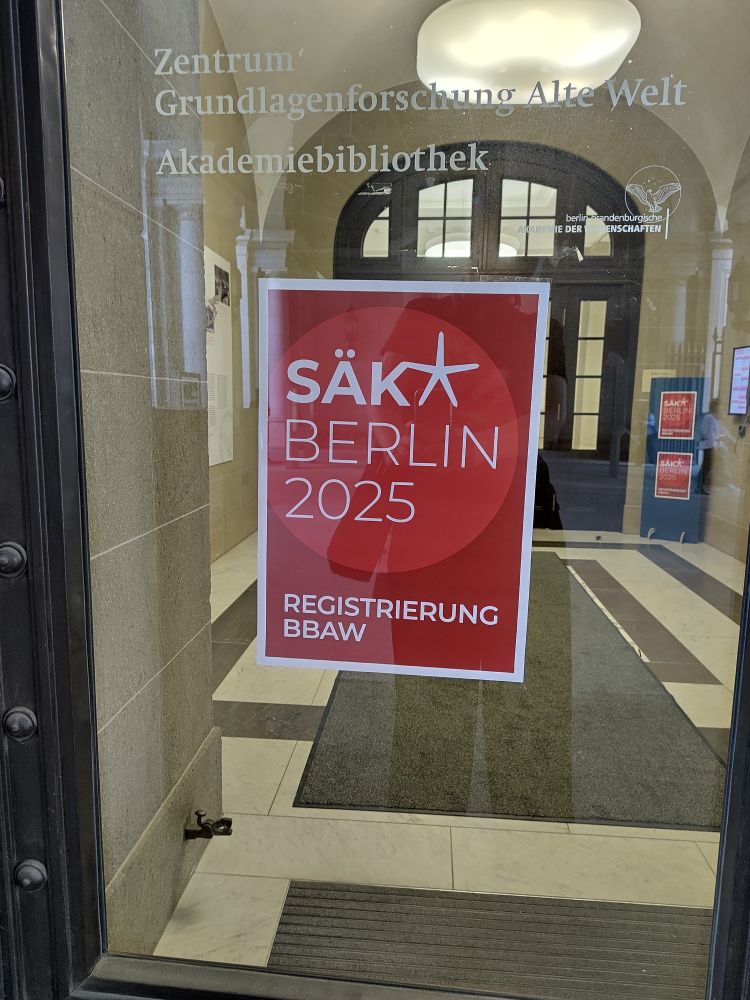 An einer Glastür hängt ein rotes Schild mit der Aufschrift SÄK* Berlin 2025 Registrierung BBAW
