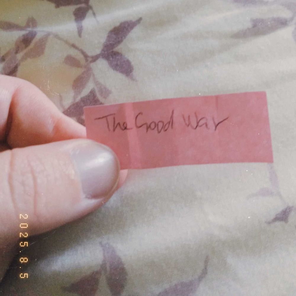 my hand holding a pink piece of paper reading "the good war" 