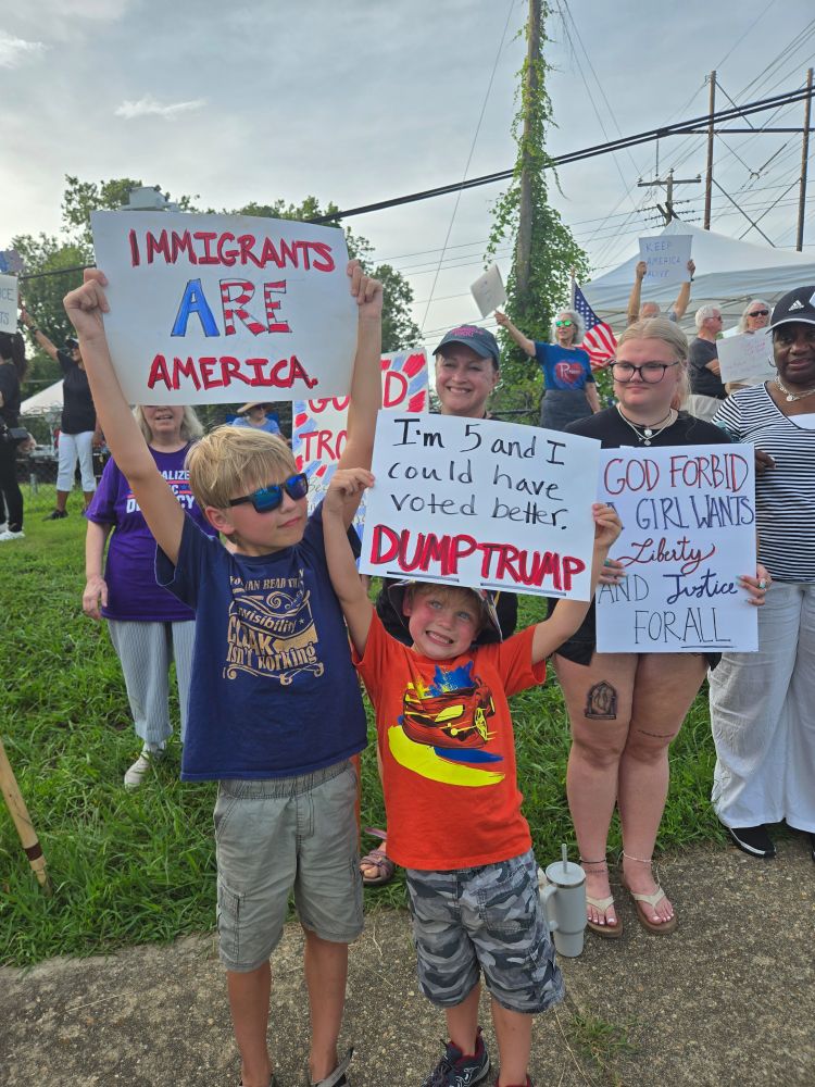 Two children hold protest signs that say IMMIGRANTS ARE AMERICA and I'M 5 AND I COULD HAVE VOTED BETTER DUMP TRUMP