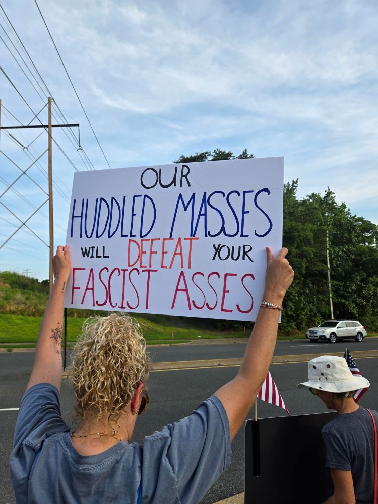 A person holds a protest sign that days OUR HUDDLED MASSES WILL DEFEAT YOUR FASCIST ASSES