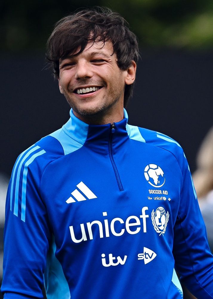 Louis Tomlinson smiling at the camera in his blue UNICEF kit.