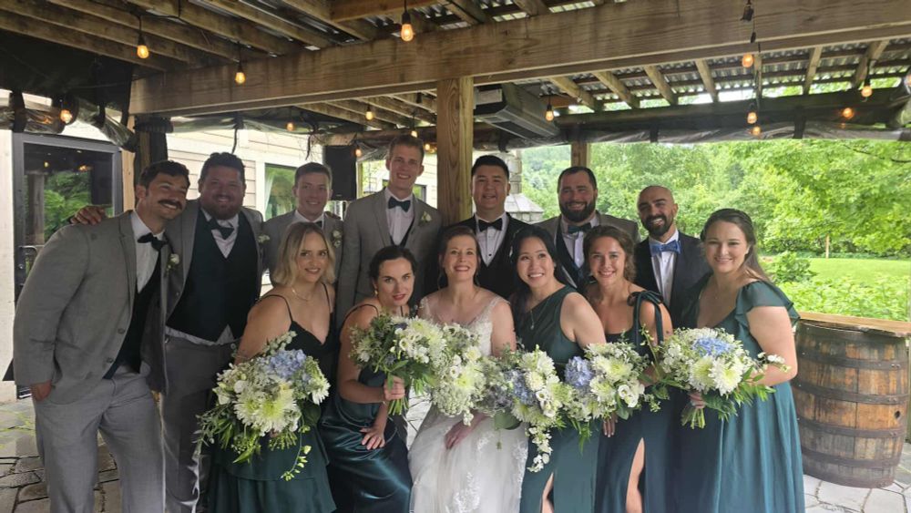 A bride, a groom, and ten grromsmen/bridesmaids pose for a group photo holding bouquets under a wooden lattice