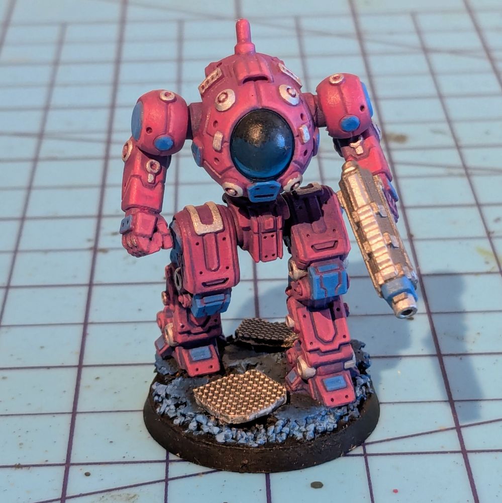 A mech miniature with a large lens walking over ruined scrap metal. It has folding legs and a blaster
