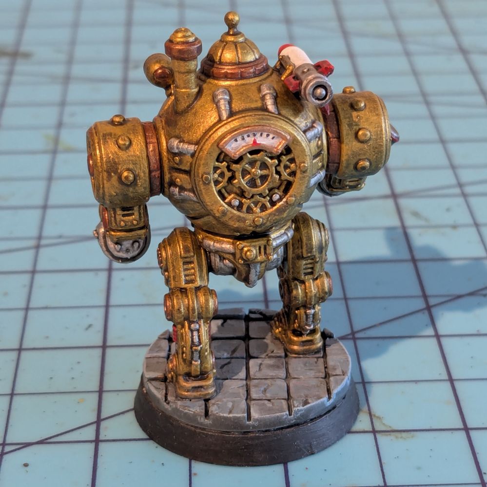 The back of a steampunk mech miniature. It has exposed gears in the back and a smokestack. 