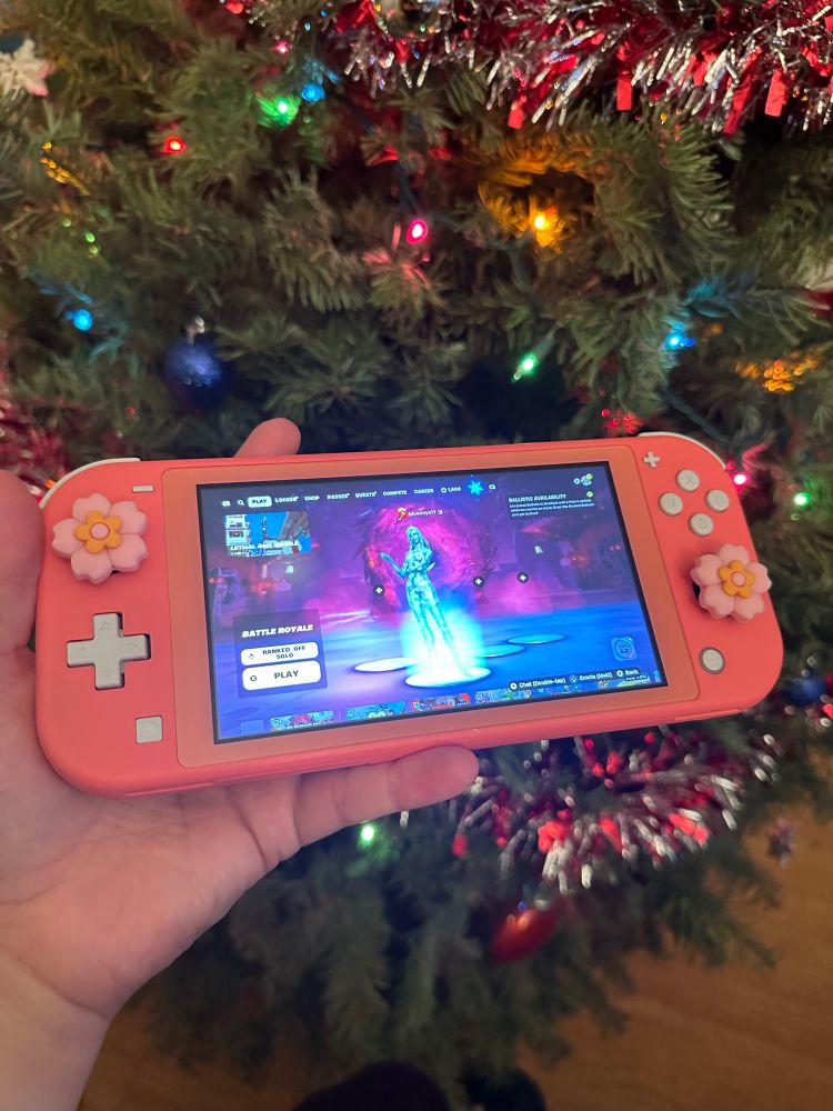 My pink nintendo switch (lite) with pink flower 🌸 grip covers. Background: Christmas tree 🎄 