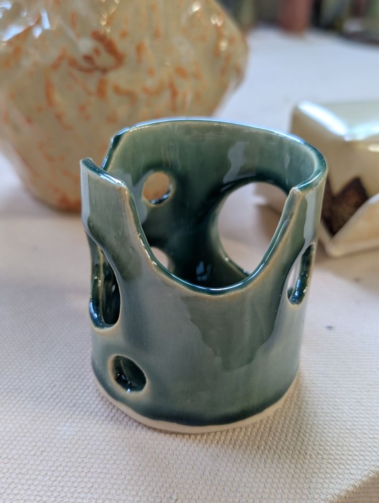 A cylindrical ceramic candle holder with circles cut out, blue-green glaze