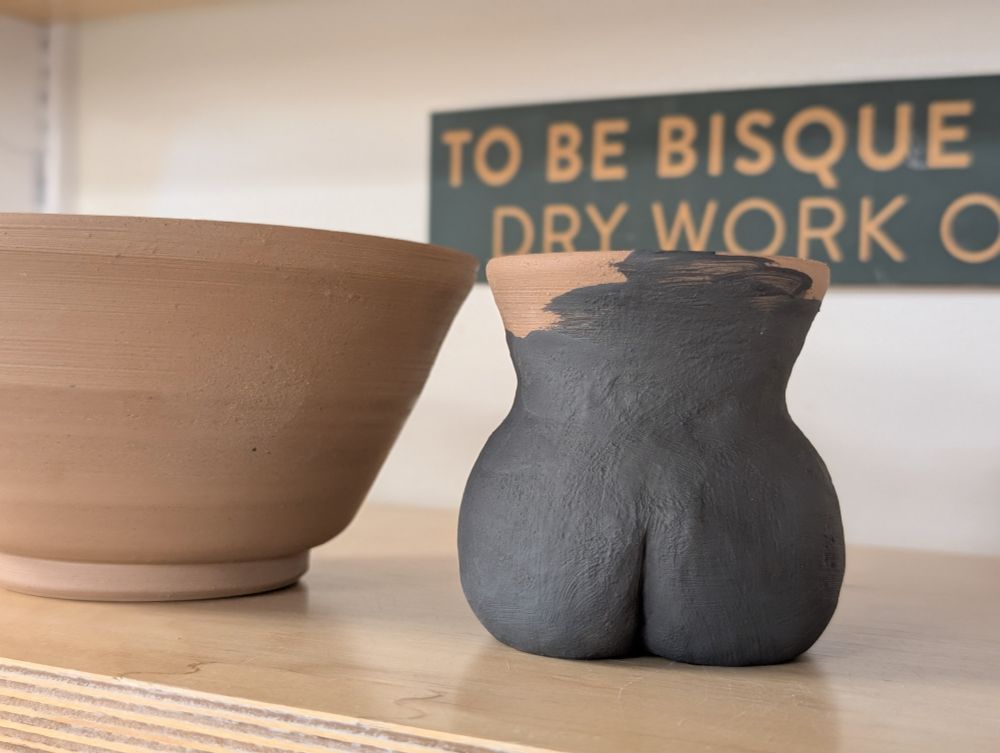 A picture of pottery pieces on a shelf with particular emphasis on a mug that looks like a sitting butt 